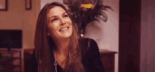 a woman with long hair is smiling in a living room in front of a vase of flowers .