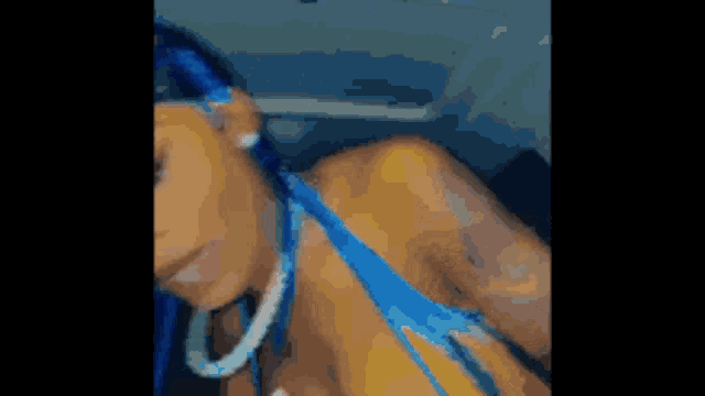a woman with blue hair and hoop earrings is wearing a blue bikini top and earrings .