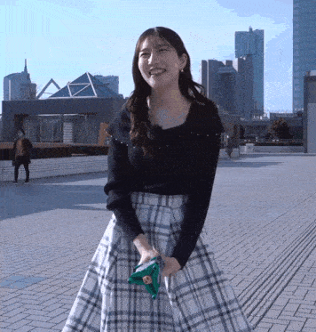 a woman in a black top and plaid skirt holds a green object
