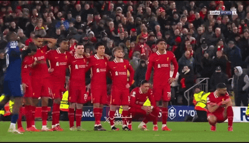 a group of soccer players are kneeling on the field while a player jumps in the air .