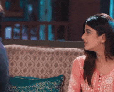 a woman in a pink top is sitting on a couch talking to a man .
