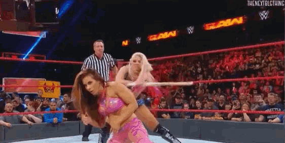 two women are wrestling in a wrestling ring with a referee in the background .