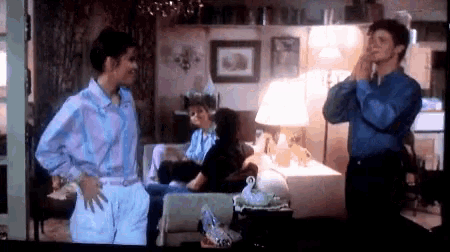 two men are standing in a living room with a woman sitting on a couch in the background