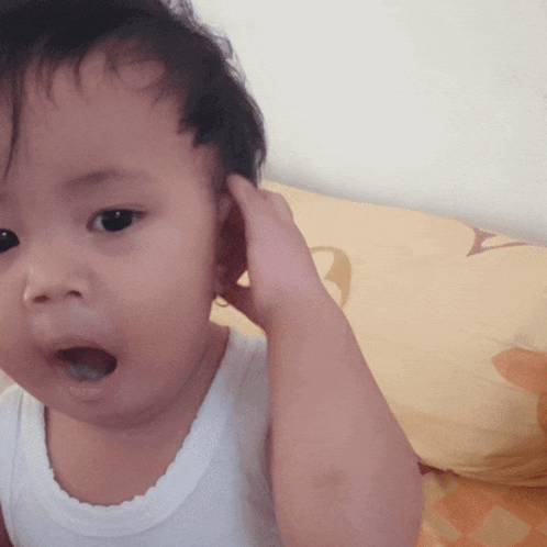 a baby with a surprised look on his face holds his hand to his ear