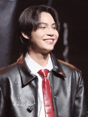 a man wearing a black jacket and a red tie smiles for the camera