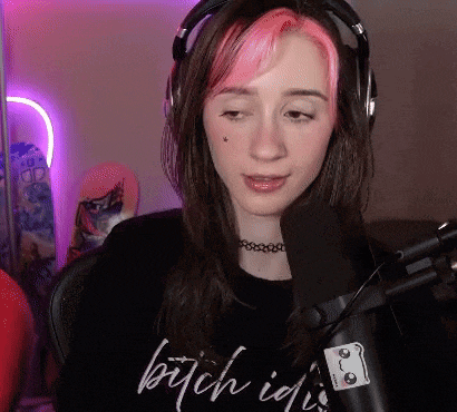 a girl with pink hair is sitting in front of a microphone wearing headphones and a choker .