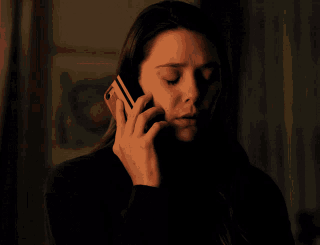 a woman in a dark room with her eyes closed holds her hand to her face