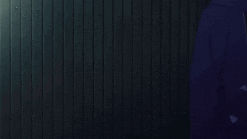 a man in a blue hoodie is standing in front of a dark wall
