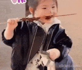a little girl is holding a toy dinosaur and eating a skewer of food .