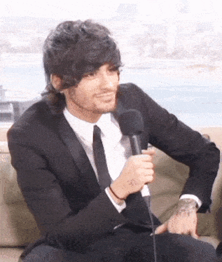 a man in a suit is sitting on a couch with a microphone in his hand