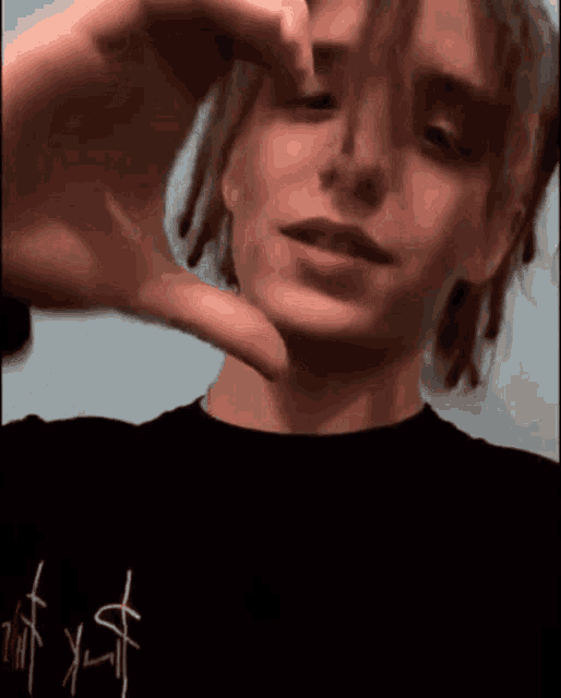 a young man with dreadlocks is making a heart shape with his hand .