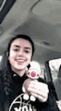 a girl is sitting in a car holding a stuffed animal and smiling .