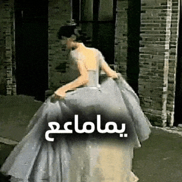 a woman in a white dress is walking in front of a brick building