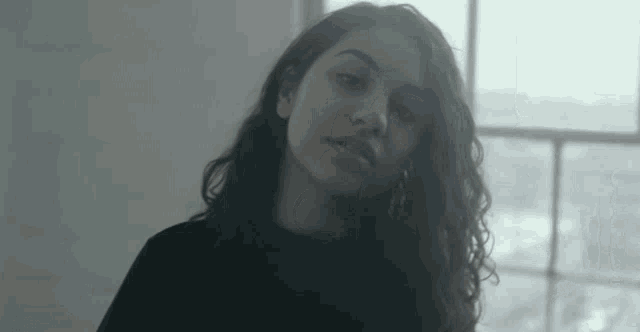 a woman with long curly hair is standing in front of a window .