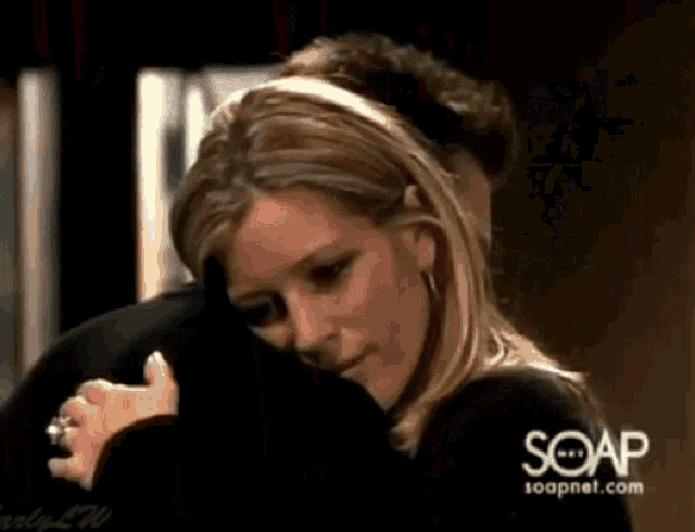 a woman is hugging a man in front of a sign that says soapnet.com .