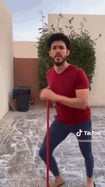 a man in a red shirt and blue pants is dancing with a broom and a tiktok sticker