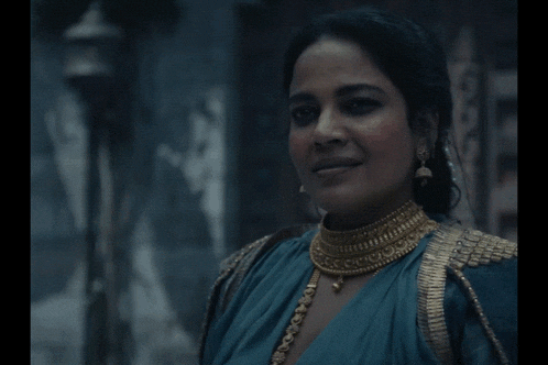 a woman wearing a blue top and gold jewelry smiles