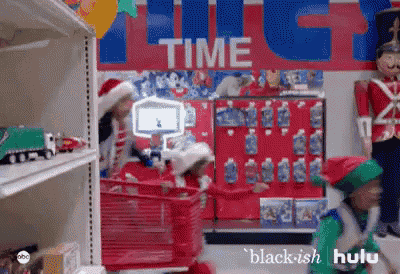 two elves are pushing a red shopping cart in a store .