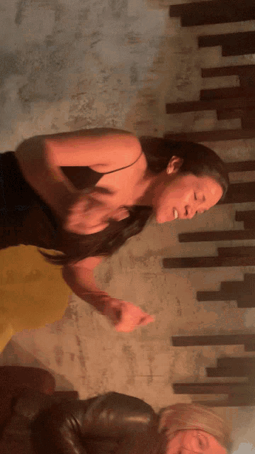 a woman in a black tank top is dancing in front of a wall
