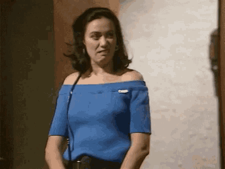 a woman in a blue off the shoulder top is standing in front of a wall