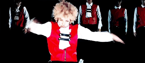 a man in a red vest is dancing in front of a group of men in white shirts .