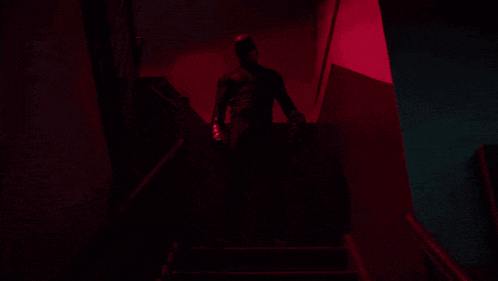 a man in a black suit is walking up a set of stairs in a dark room