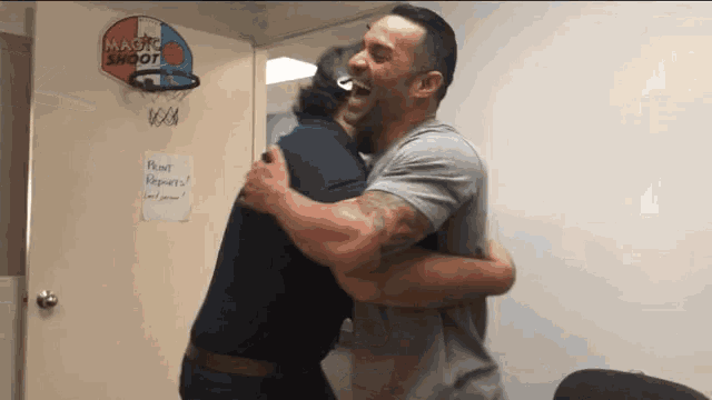 two men are hugging in front of a magic shoot sign