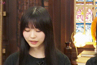 a young woman with long black hair is sitting in front of a stained glass window .