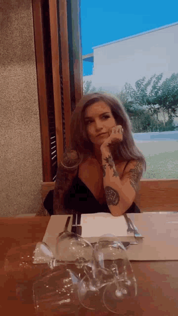a woman with tattoos sits at a table with glasses on it