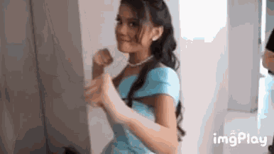 a woman in a blue dress is standing in front of a mirror and making a fist .