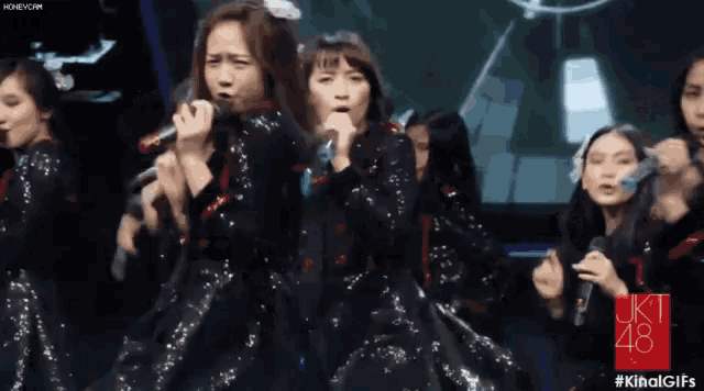 a group of girls singing into microphones with the number 48 on the bottom left