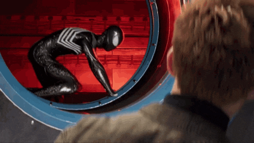 a man in a suit looks through a window at a spider man in a black suit with the words stay positive written on it