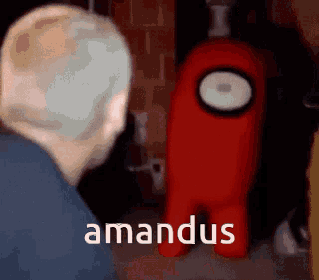 a man is standing in front of a red among us character with the word amandus written on it .