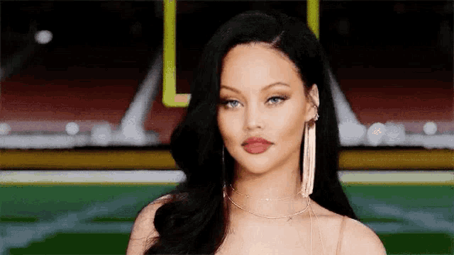 a close up of a woman wearing earrings and a necklace standing in front of a football field .