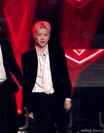 a man in a suit and white shirt is dancing on a stage in front of a red background .