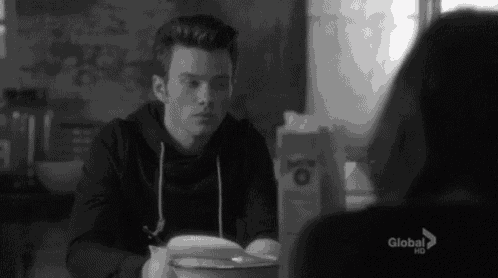 a man is reading a book while sitting at a table with a woman .