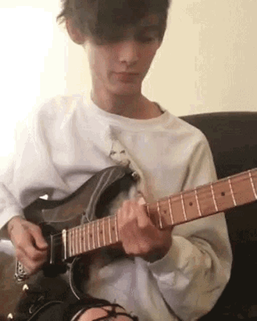 a young man is playing a guitar in a chair .