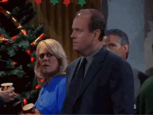 a man in a suit is standing in front of a christmas tree