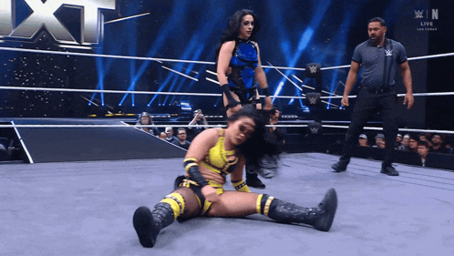 a female wrestler is laying on the ground in a wrestling ring while another wrestler stands behind her