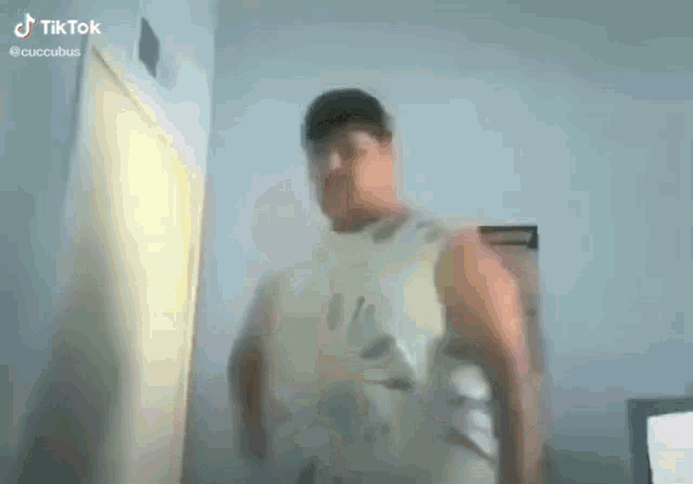 a man in a white tank top is standing in a room in front of a door .