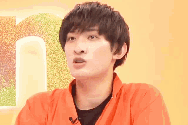 a young man wearing an orange shirt and a black shirt is sitting in front of a yellow background .