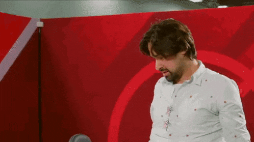 a man in a white shirt is standing in front of a red wall .