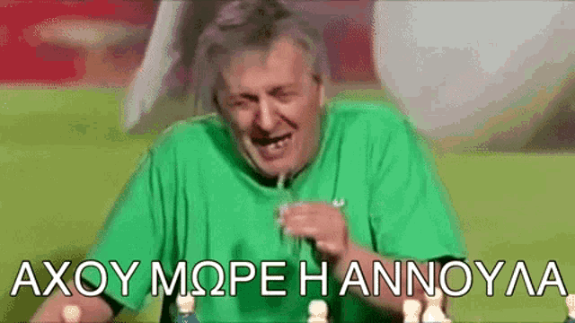 a man in a green shirt is sitting at a table drinking from a glass .