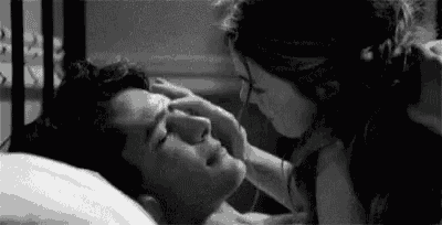 a black and white photo of a woman touching a man 's face in bed .