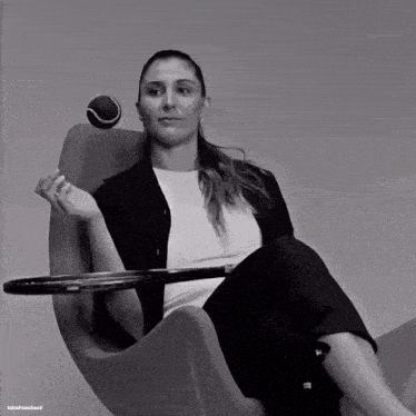 a woman is sitting in a chair holding a tennis racket and a tennis ball in her hand