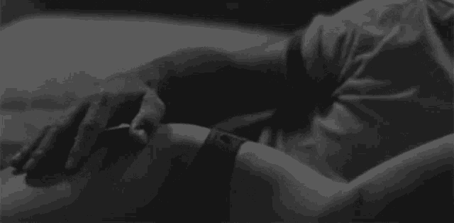 a black and white photo of a man and a woman holding hands while laying on a bed .