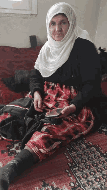 a woman wearing a white hijab sits on a rug