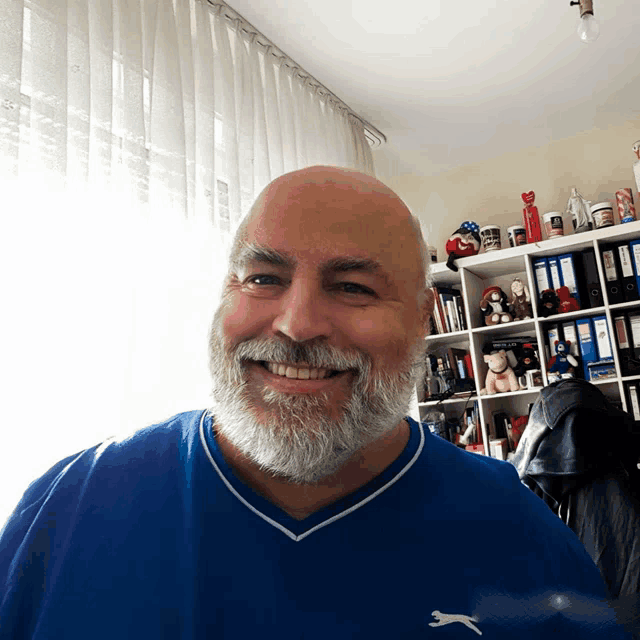 a man with a beard wearing a blue puma shirt smiles