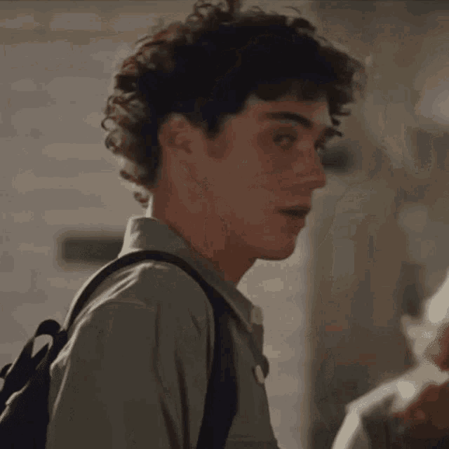a young man with curly hair is wearing a grey jacket and a white shirt .