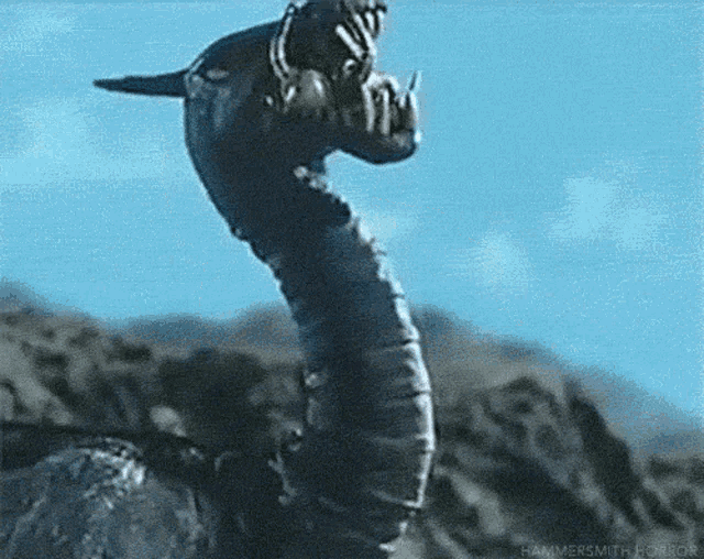 a monster with a long neck and sharp teeth is standing on top of a hill .